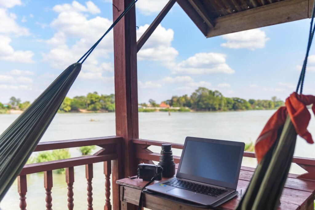 Working with laptop on wooden balcony in tourist resort with hanging hammock on the Mekong River, Laos. Concept of millenials working around the world and digital nomads.