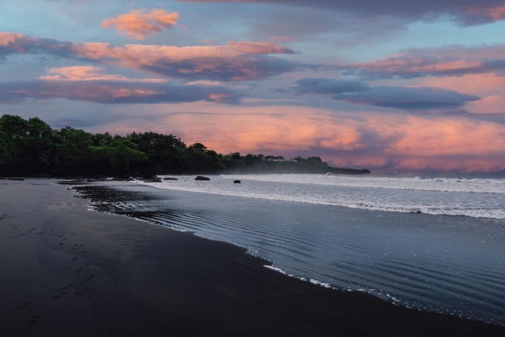 Volcanic sandy beach with ocean waves in Bali. Black sand coastline and sunset or sunrise cloudy sky
