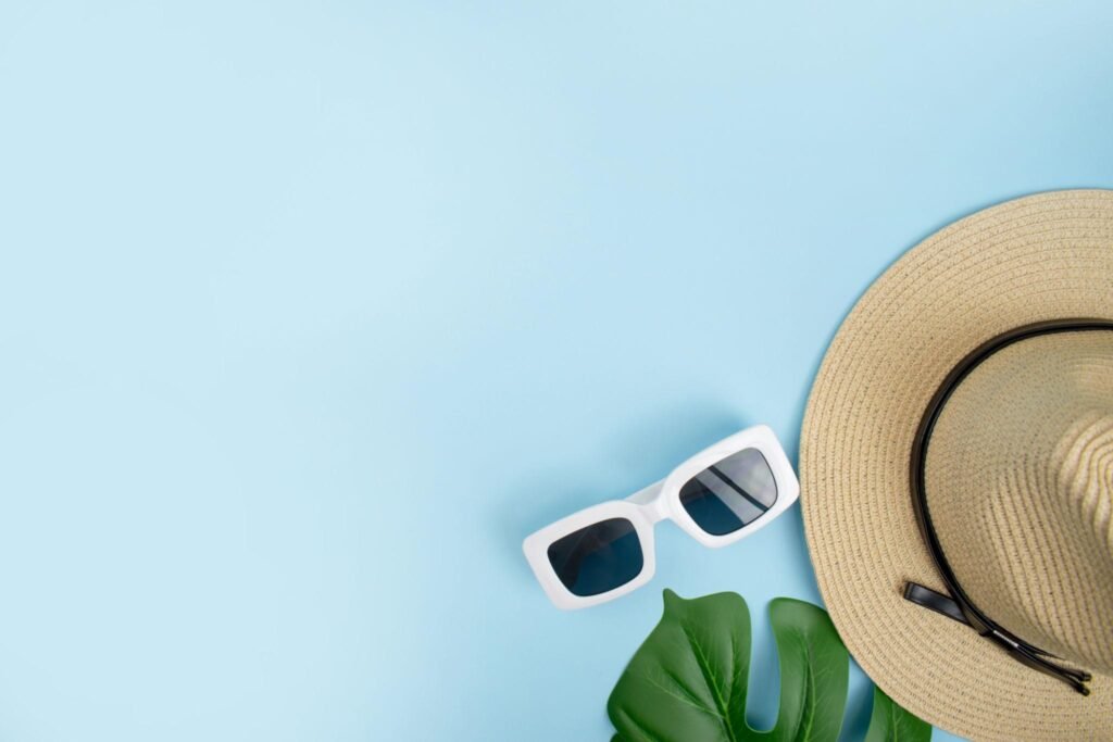 Top view of tourist accessories with hats, sunglasses and summer leaves on a blue background. with copy space.
