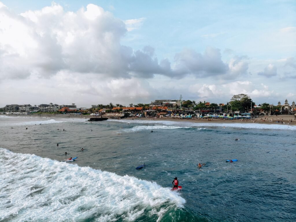 Aerial view of man on surfboard catching wave on Canggu beach located in the west of Bali on sunset with beautiful sky