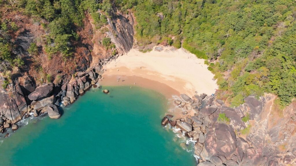 Beautiful secret beach Butterfly in Goa, India. Aerial view of pristine beach with rocky bay and waves crashing
