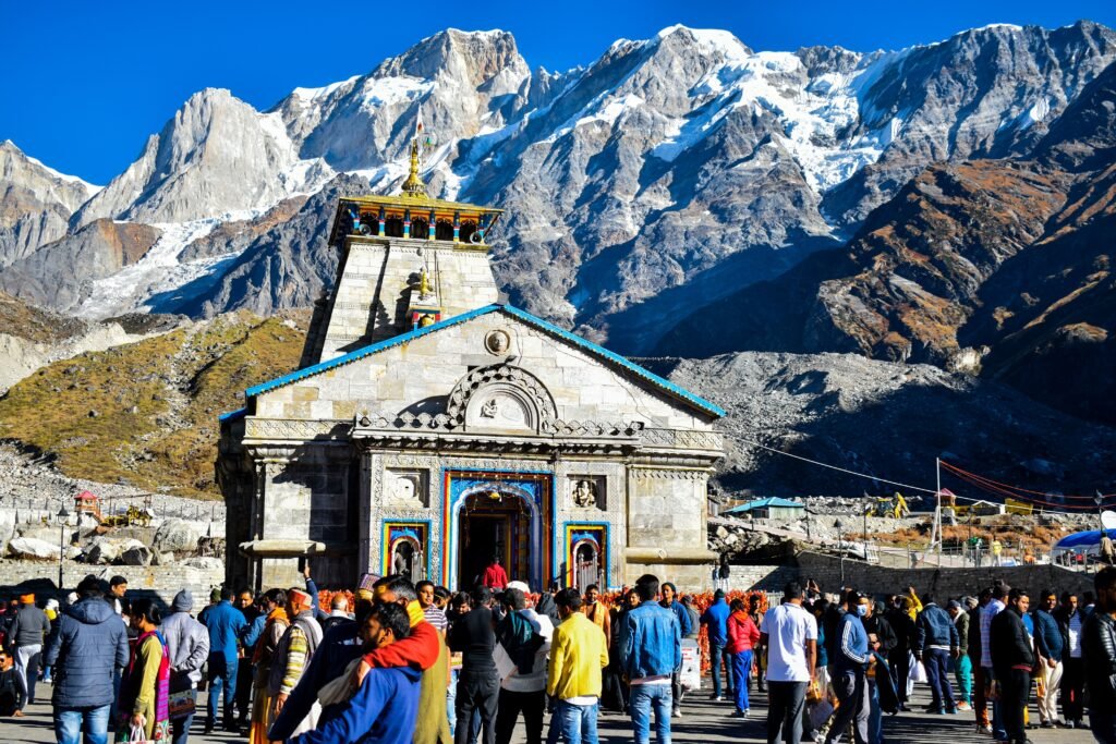Crowd gathers at Kedarnath Temple azwith Himalayas backdrop, showcasing religious significance and stunning landscape.