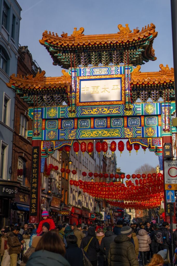 A lively scene beneath the colorful Chinese archway in London Chinatown during a festival.
