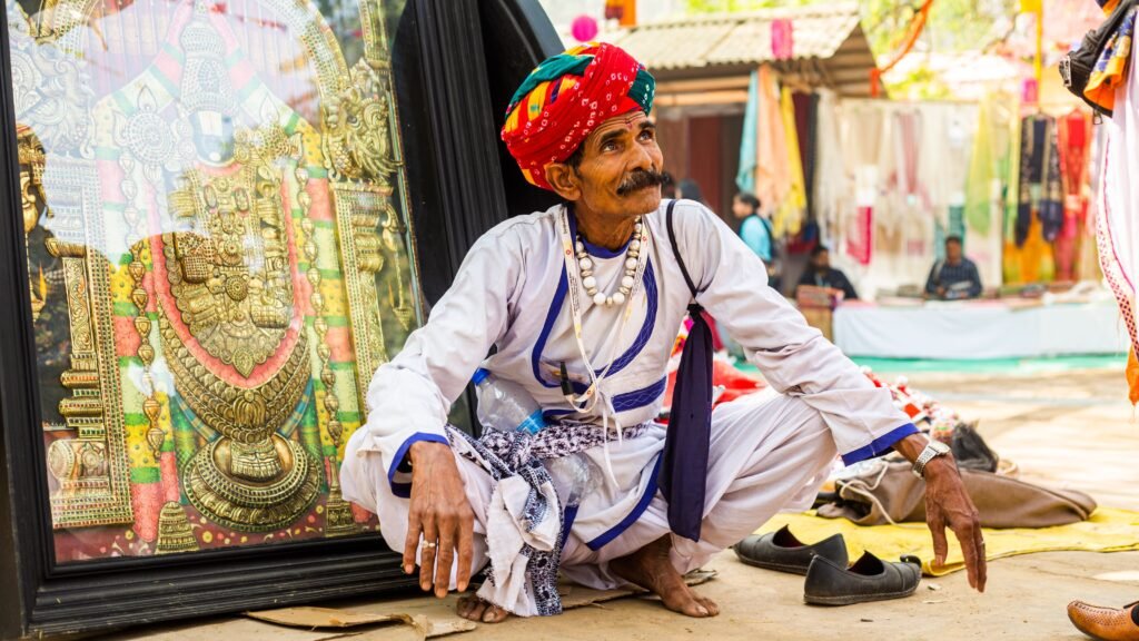 Elderly man wearing vibrant turban and traditional clothing at an outdoor bazaar.