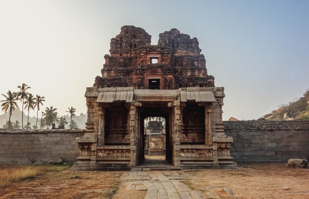Majestic ancient temple ruins in Hampi, India, captured at sunrise with palm trees in the background.