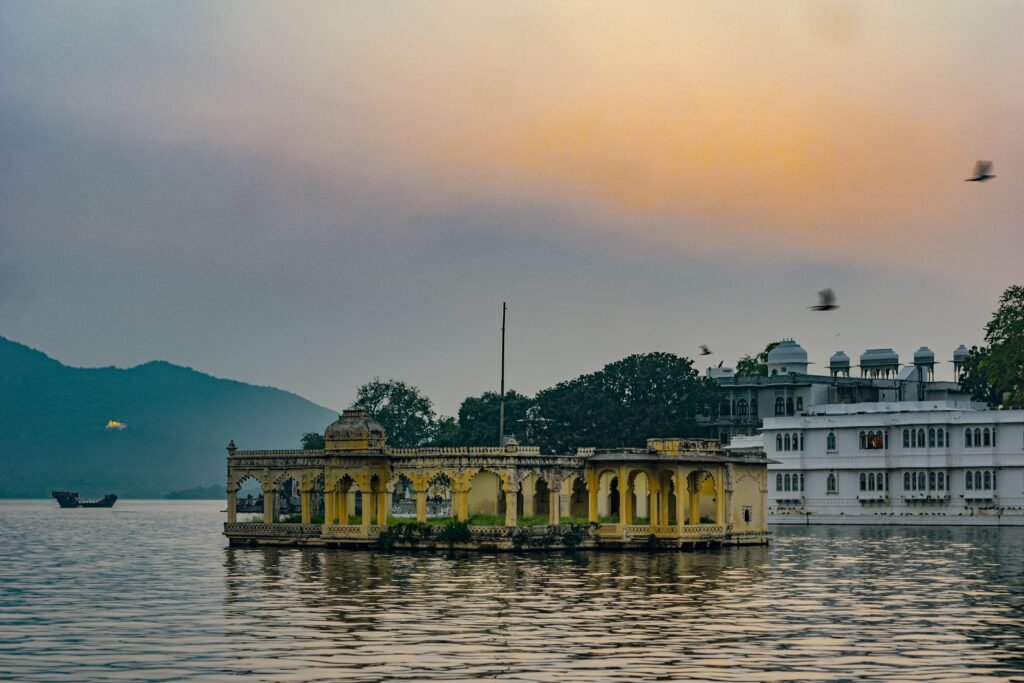 A serene view of a Lake Palace in India with a vibrant sunset sky and birds in flight.
