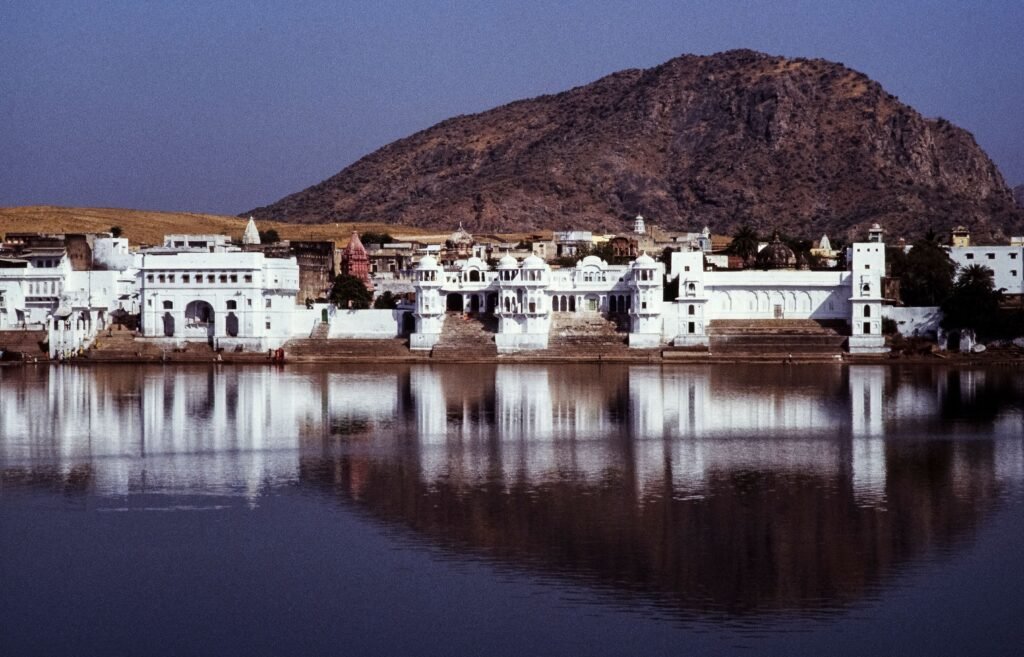 Reflective view of Pushkar Lake with surrounding architecture and hills in India.