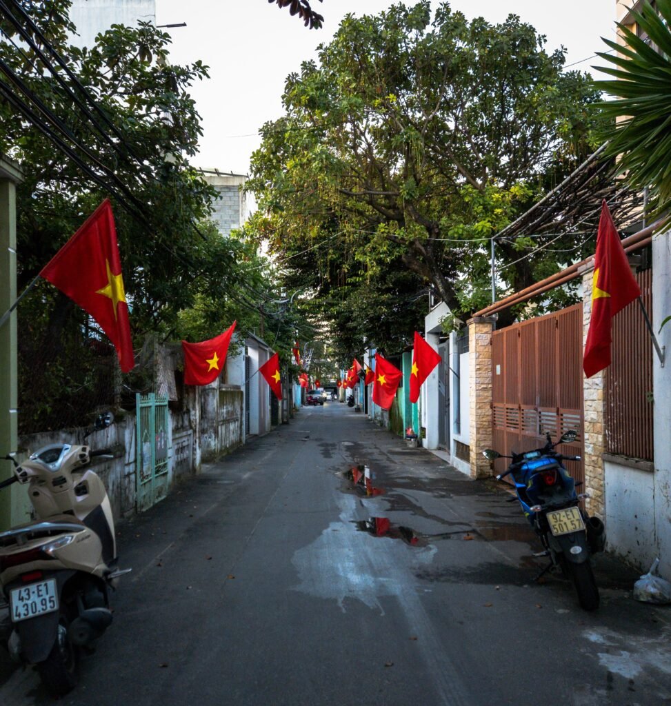 Quiet Vietnamese city alley lined with red national flags, showcasing local pride.
