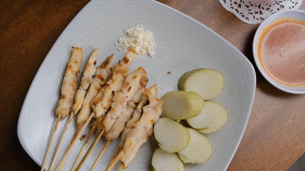 Tasty Indonesian chicken satay skewers served with sauce and rice cakes on a plate.