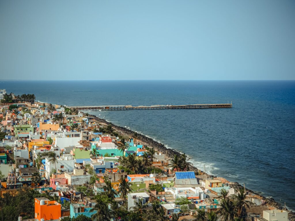 A vibrant aerial view of Puducherry with colorful houses by the sea and a prominent pier.