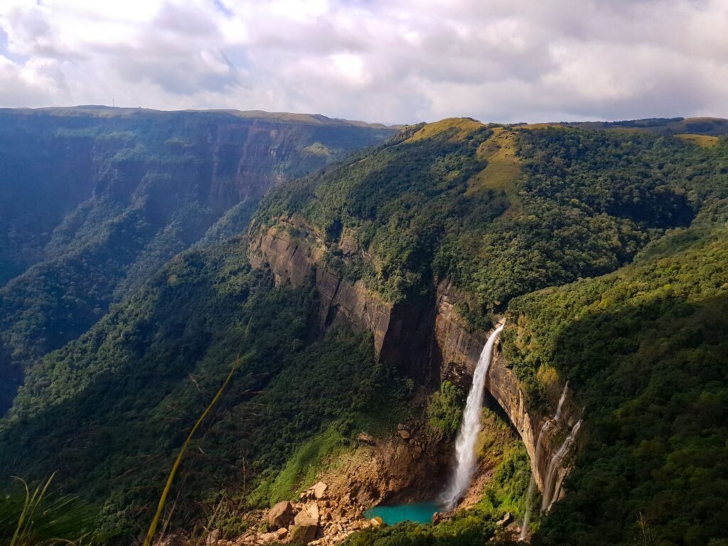 A breathtaking aerial view of a waterfall cascading down lush green hills in Meghalaya, India.
