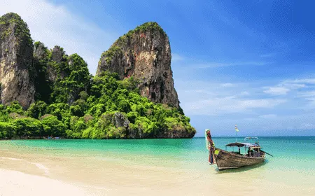 Traditional long-tail boat anchored on a white sand beach with limestone cliffs and turquoise water in Krabi, Thailand