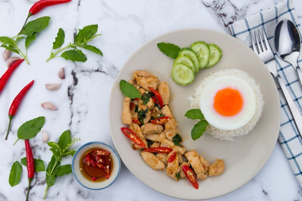 A vibrant Thai meal featuring basil chicken, rice, and a sunny-side-up egg.