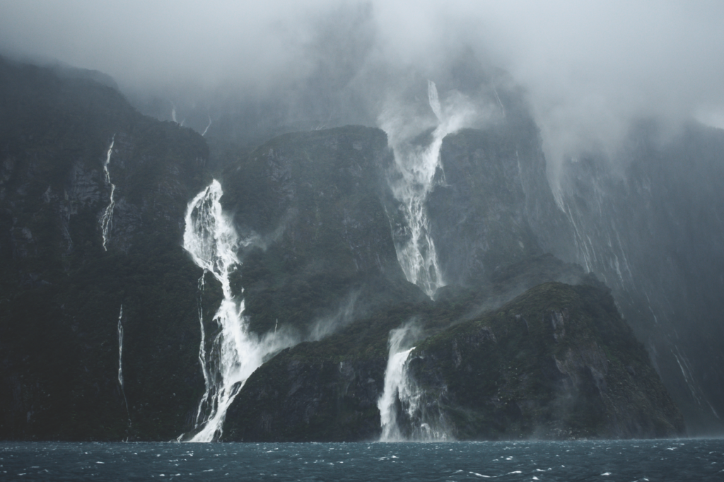 Stunning waterfalls cascade down misty cliffs in a dramatic fjord setting.