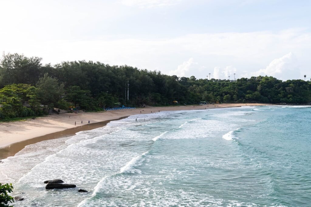 A serene beach with gentle waves and lush greenery in Phuket, Thailand.