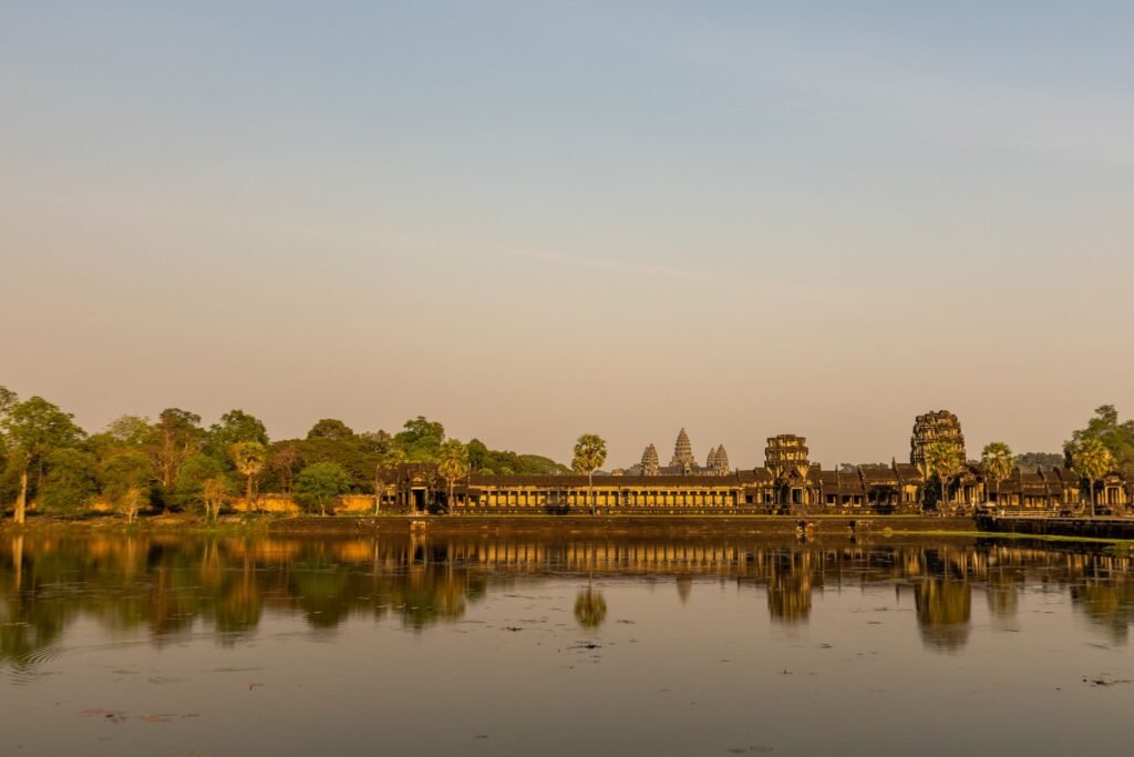 Majestic Angkor Wat temple reflecting in calm waters at sunrise, showcasing ancient architecture.