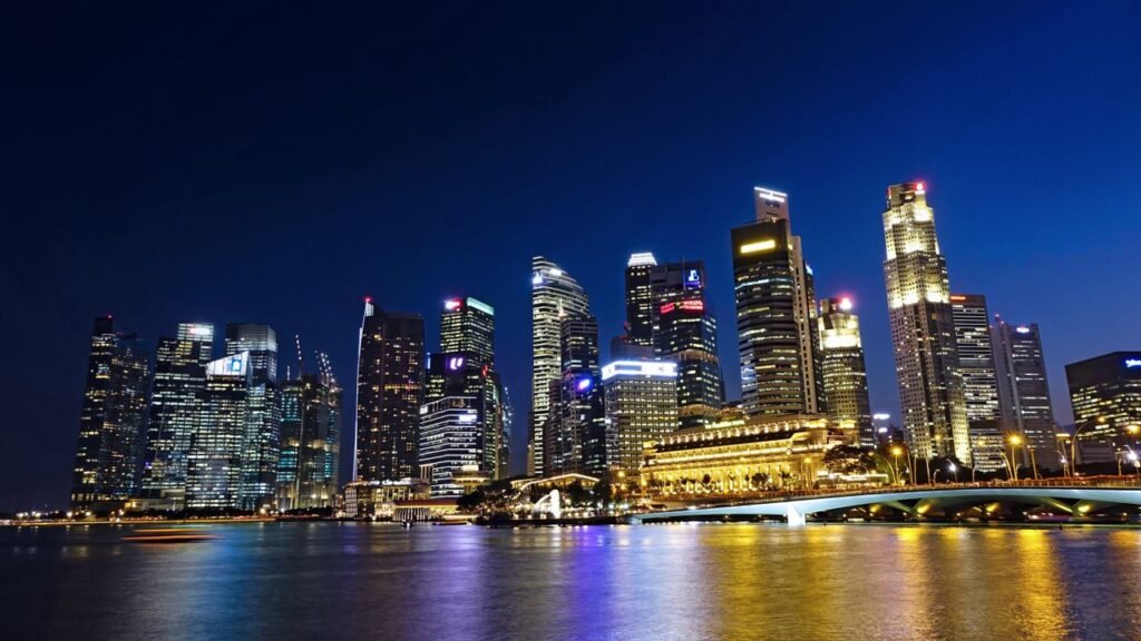 Vibrant night view of Singapore city skyline with illuminated skyscrapers reflected in water.