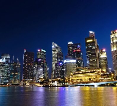 Vibrant night view of Singapore city skyline with illuminated skyscrapers reflected in water.
