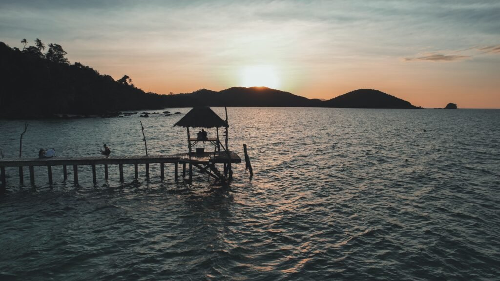 Scenic sunset view at a wooden pier in Ko Mak, Thailand, overlooking the sea and hills.
