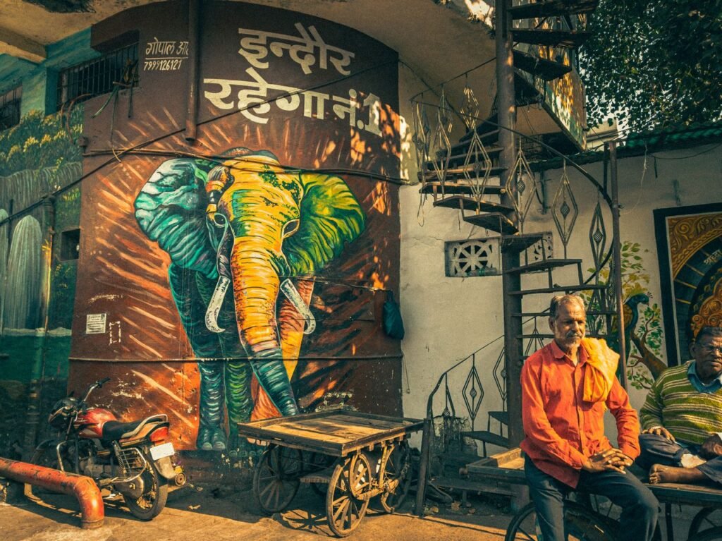 Vibrant street art featuring an elephant mural in Indore, India, with local men and a spiral staircase.