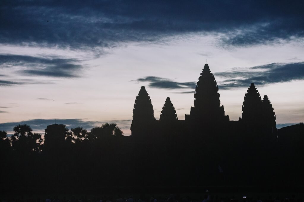 Silhouette of Angkor Wat temple at dusk with dramatic sky.
