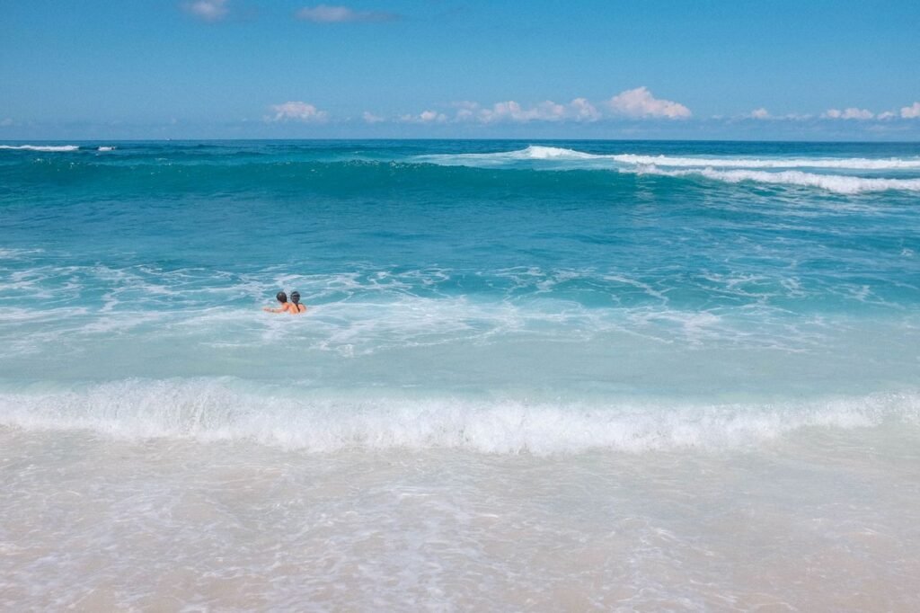 Two people enjoy a swim in the serene, turquoise ocean off a beautiful Bali beach.