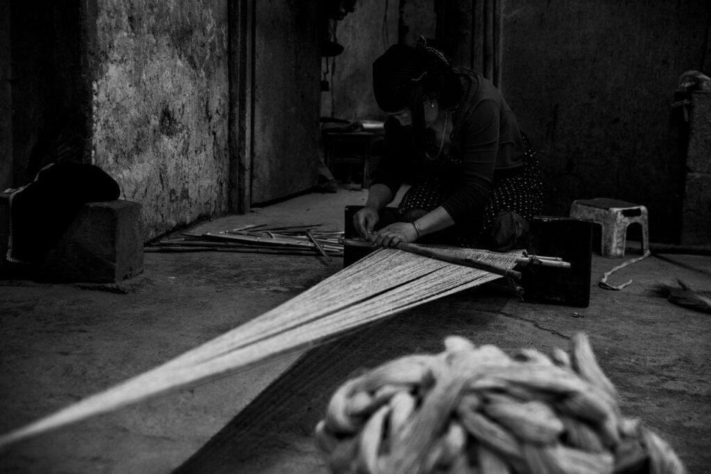 Artistic image of a woman weaving textile in monochrome, showcasing traditional craftsmanship.