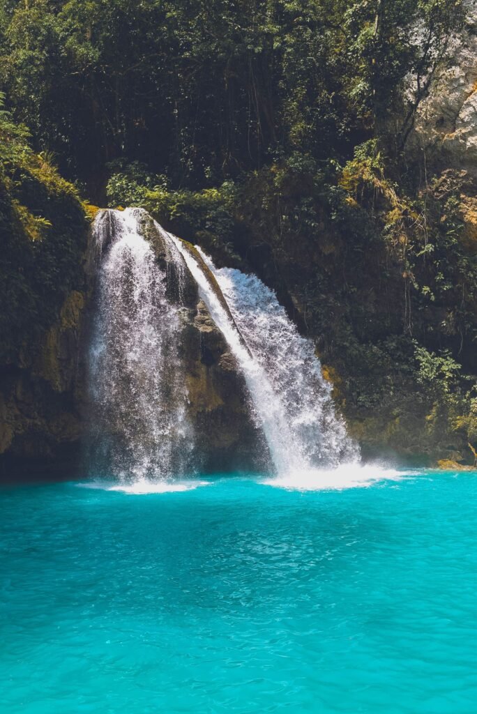 A tranquil waterfall cascading into a vibrant blue pool surrounded by lush greenery.