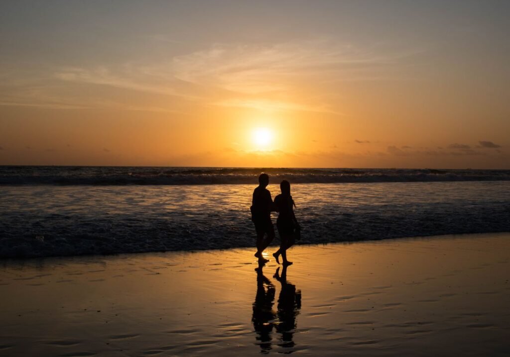 Couple enjoying a romantic walk on Kuta Beach, Bali during a stunning sunset.