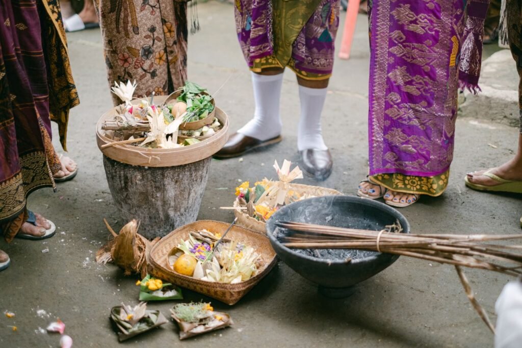 People in traditional attire gather for a Balinese offering ceremony with flowers and fruits.