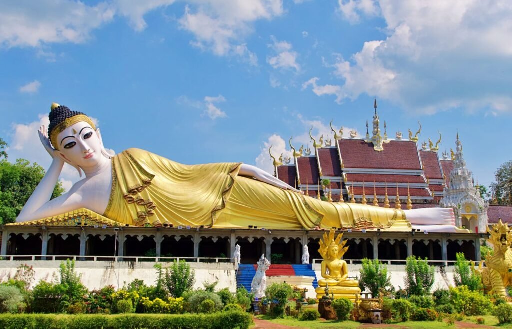 Stunning view of a golden Reclining Buddha statue against a vivid blue sky in Thailand's beautiful temple grounds.