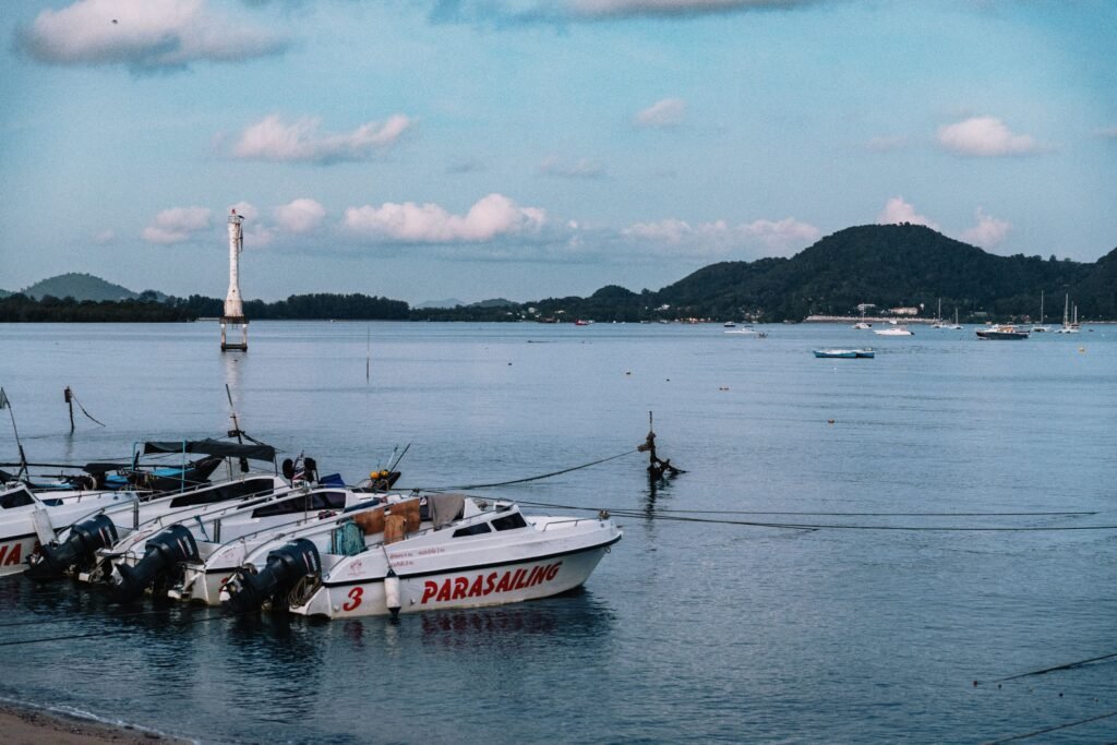 Parasailing boats anchored at a serene Phuket beach with a lighthouse view.