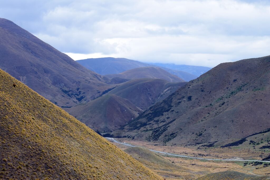Panoramic view of the rolling hills and valleys in Otago, New Zealand, under a cloudy sky.