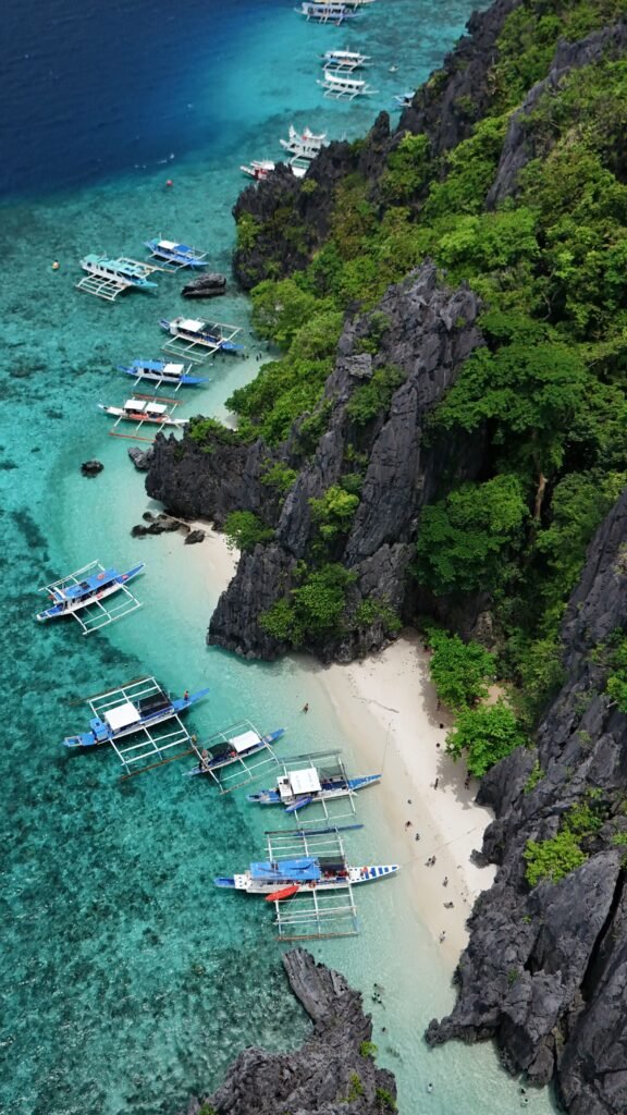 Aerial shot of vibrant boats along the lush, rocky coastline of Coron, Philippines.