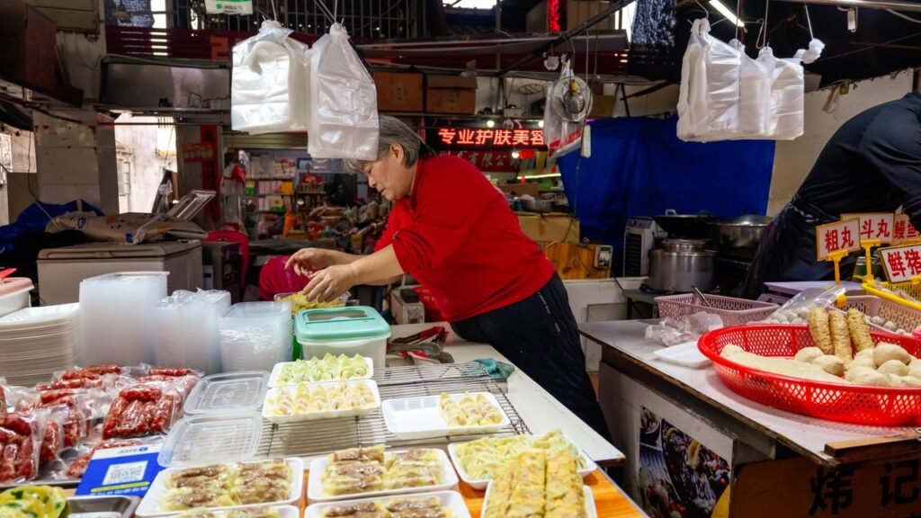 A street vendor in an indoor market preparing traditional Chinese dumplings and other delicacies.
