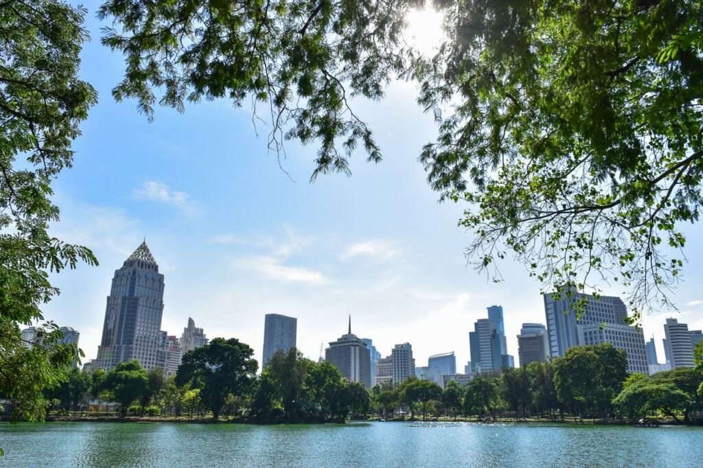 Scenic view of Bangkok's skyline from a park with lake and trees during daytime.