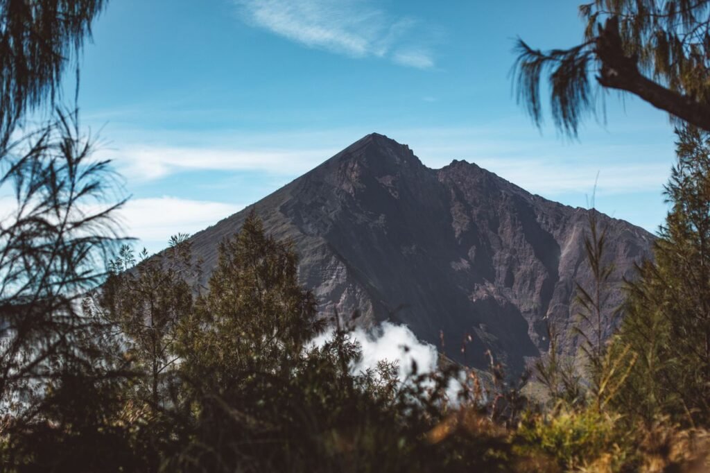 View from tropical forest of Rinjani National Park on volcanic rocky mountain towering above clouds