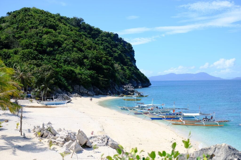 Idyllic tropical beach scene with docked boats, sandy shore, and lush green hills.