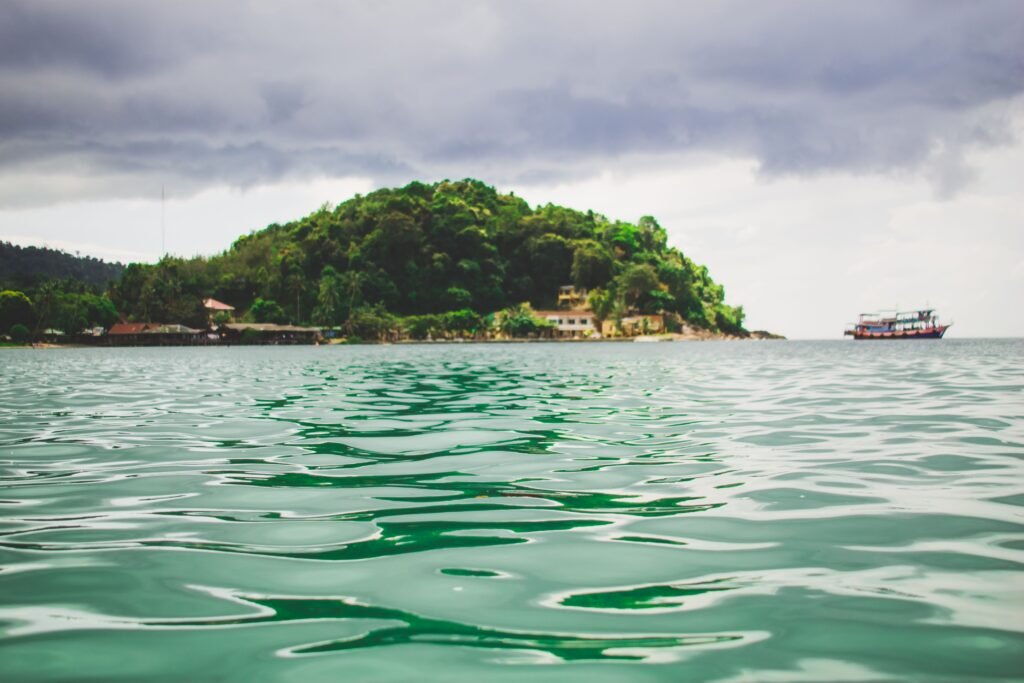 Scenic view of a lush island surrounded by green waters and a distant boat in Thailand.