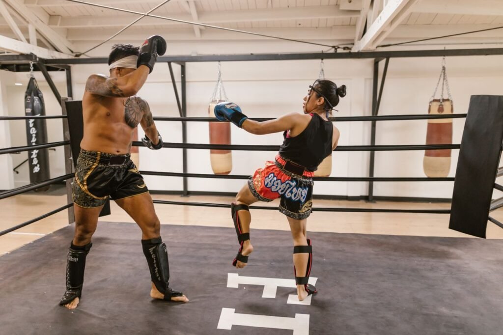 Two athletes engage in a dynamic Muay Thai sparring session inside a gym boxing ring.