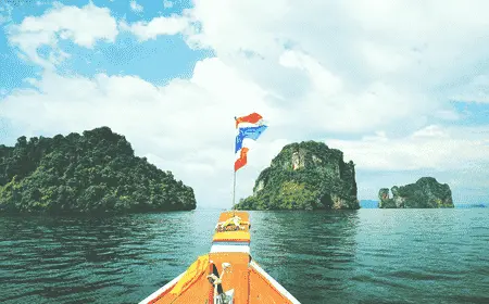 Traditional Thai long-tail boat sailing toward limestone islands in Phang Nga Bay, Thailand