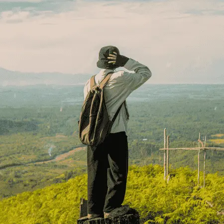 Traveler with a backpack enjoying a scenic mountain viewpoint overlooking a lush green valley in Thailand