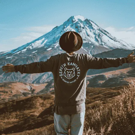 Traveler with outstretched arms facing a snow-capped mountain during an outdoor adventure