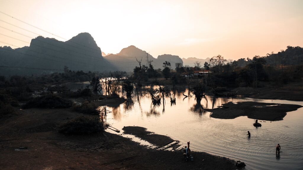 Peaceful sunset view of a lake with mountain backdrop in Laos, reflecting serene beauty and nature's tranquility.