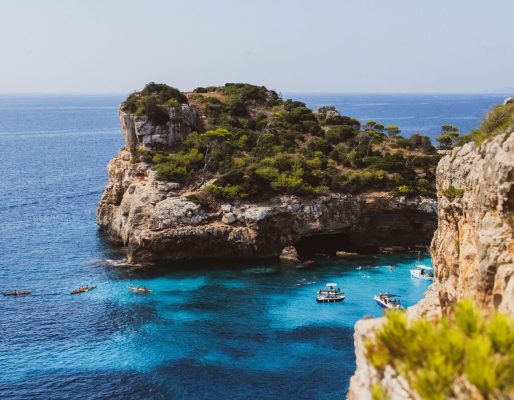 A stunning view of a rocky island cliff surrounded by turquoise Mediterranean waters and boats.