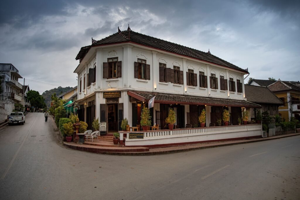 Elegant colonial-style building at a street corner in Luang Prabang, Laos, under cloudy skies.