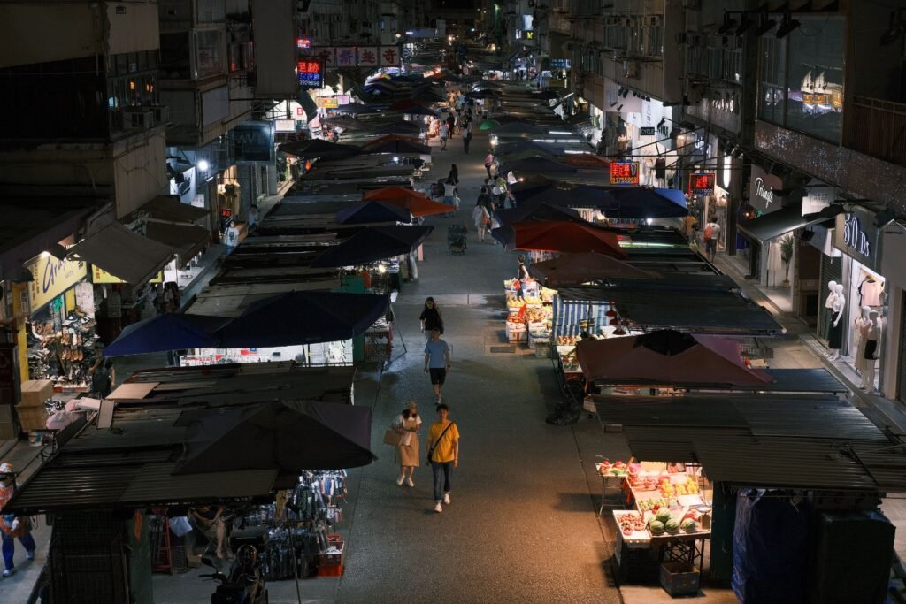 Bustling night market street with vibrant stalls and pedestrians in an urban setting.