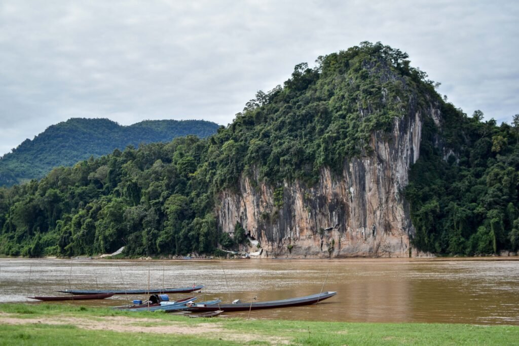 Longboats on the Nam Ou River with lush forested cliffs in Luang Prabang, Laos.