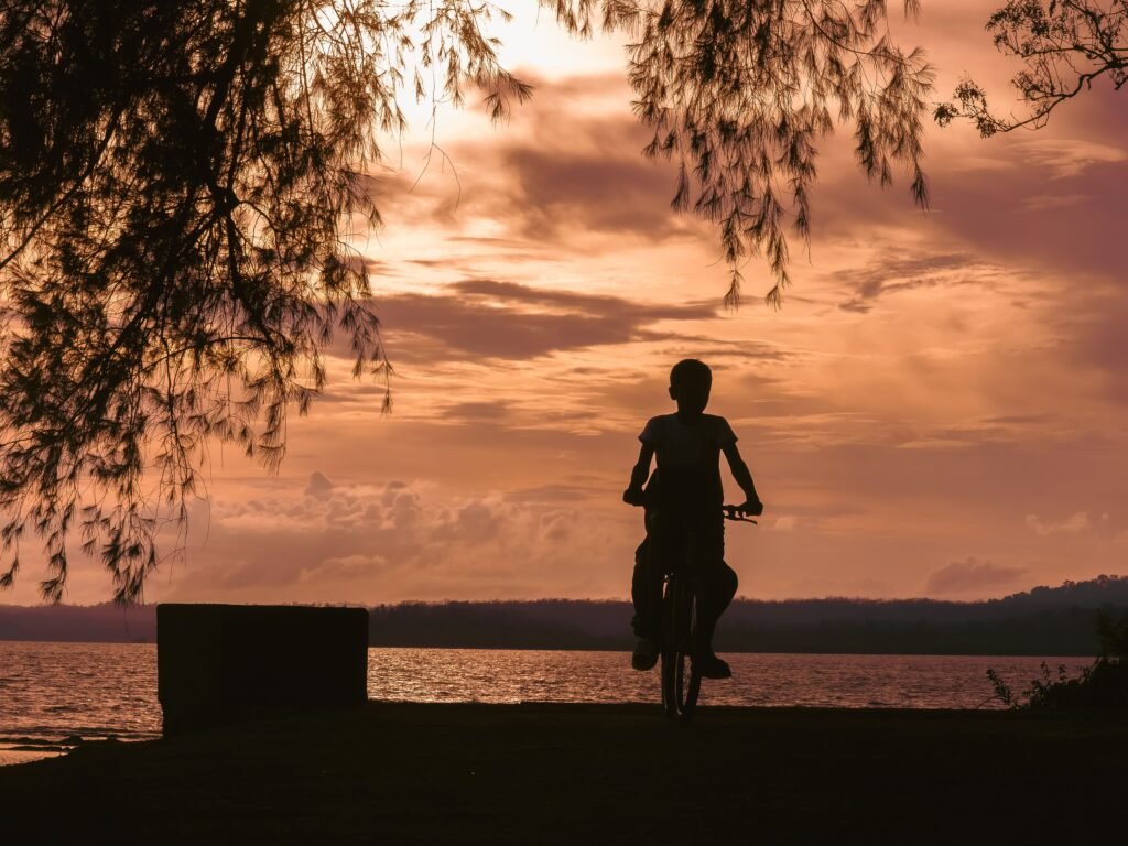 A child rides a bicycle silhouetted against a stunning sunset on an Andaman beach, India.