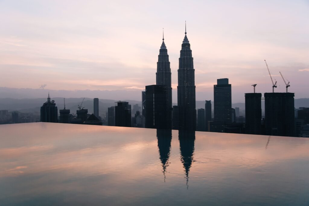 Silhouette of Petronas Towers in Kuala Lumpur reflected in infinity pool at sunset.